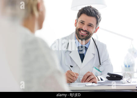 Smiling doctor discussing with mature patient while writing prescription at desk in hospital Stock Photo