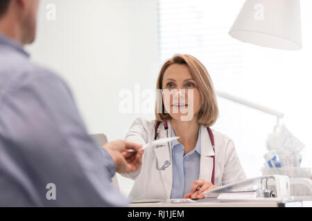 Smiling doctor giving prescription to patient at desk in hospital Stock Photo