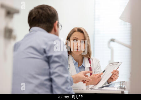 Doctor explaining prescription on clipboard to patient at desk in hospital Stock Photo