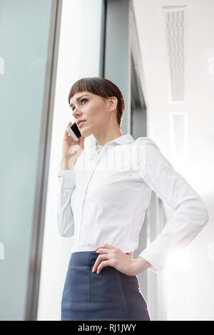 Businesswoman talking on smartphone while standing by window at office Stock Photo