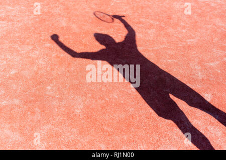 Shadow of successful man standing with arms raised on red tennis court during match Stock Photo