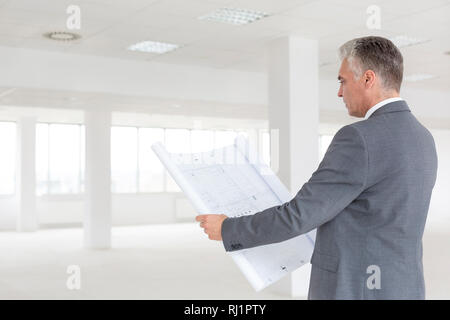 Mature businessman looking at blueprint while standing in new empty office Stock Photo