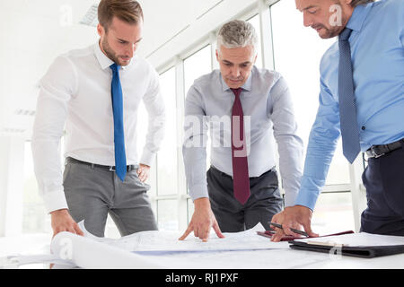 Businessmen analyzing blueprints at table in new office Stock Photo