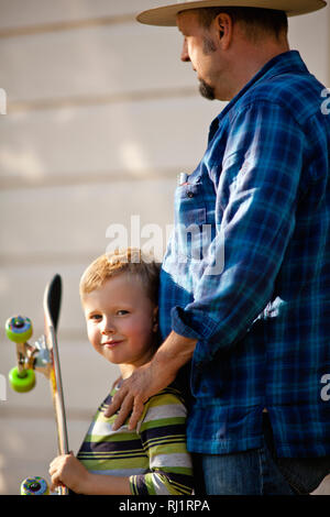 Little boy standing next to his father and holding his skateboard. Stock Photo