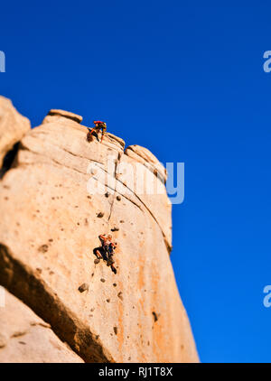 Low-angle view of two rock climbers climbing on mountain top. Stock Photo