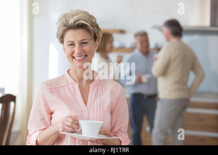 Portrait smiling mature woman holding drink while standing against friends at home Stock Photo