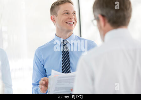 Smiling business colleagues discussing over document by wall at office Stock Photo