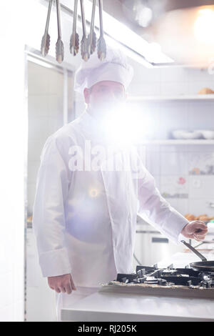 Backlit mature chef standing at kitchen counter in restaurant Stock Photo