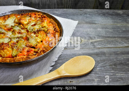Pie with vegetables and cheese in a vintage pan with a wooden spoon on a white linen napkin on wooden rustic background Stock Photo