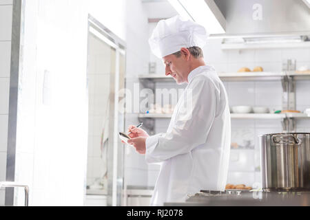 Side view of chef writing on notepad while standing in kitchen at restaurant Stock Photo