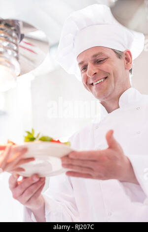 Smiling chef giving salad plate to waiter in kitchen at restaurant Stock Photo