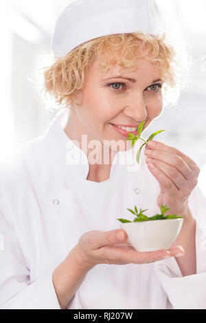 Closeup of confident chef smelling fresh mint leaves in kitchen at restaurant Stock Photo