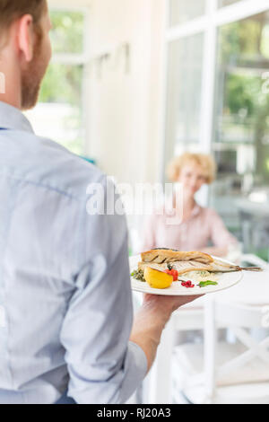 Waiter serving lunch to mature customer sitting at table in restaurant Stock Photo