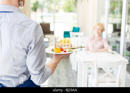 Midsection of waiter serving lunch to mature customer sitting at table in restaurant Stock Photo