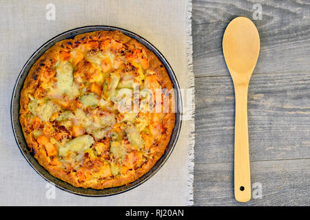 Pie with vegetables and cheese in a vintage pan with a wooden spoon on a white linen napkin on wooden rustic background Stock Photo