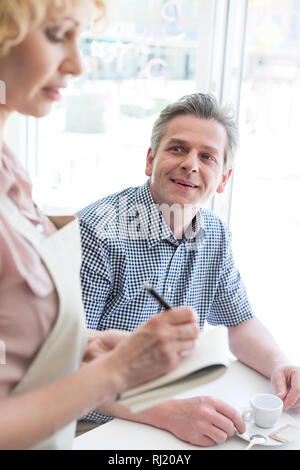 Man looking at waitress writing order on notepad at restaurant Stock Photo