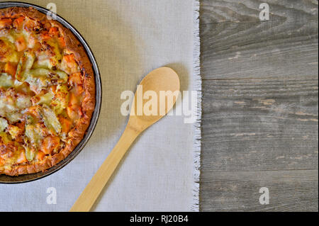Pie with vegetables and cheese in a vintage pan with a wooden spoon on a white linen napkin on wooden rustic background Stock Photo