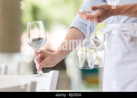 Midsection of young waiter arranging wineglasses on table in restaurant Stock Photo