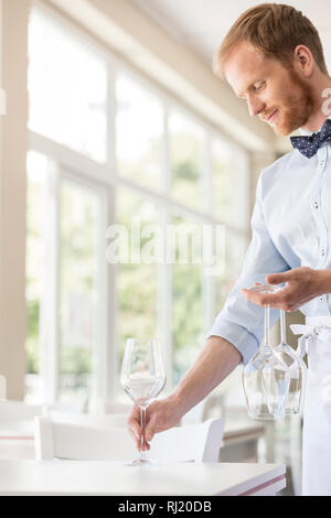 Young waiter arranging wineglasses on table at restaurant Stock Photo