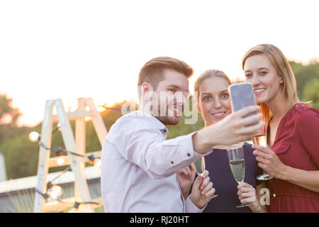 Young businessman taking selfie with colleagues during rooftop party Stock Photo