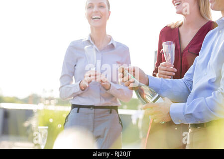 Mature businessman opening wine bottle by colleagues during rooftop party Stock Photo