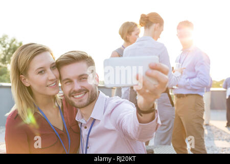 Smiling young businessman and businesswoman taking selfie at party on rooftop Stock Photo