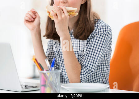 Midsection of businesswoman eating sandwich while working in office Stock Photo