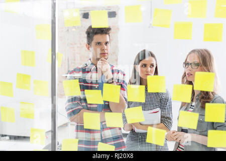 Creative business colleagues discussing over strategies on adhesive notes Stock Photo