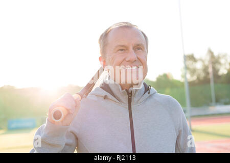 Smiling senior man standing with tennis racket on court against clear sky