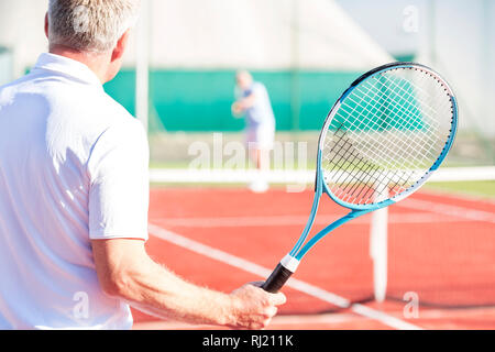 Rear view of mature man holding racket while playing with friend on tennis court Stock Photo