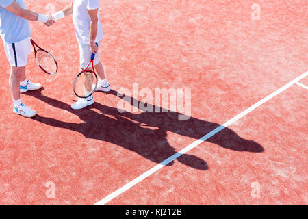 Low section of mature men shaking hands while standing on tennis court during match Stock Photo