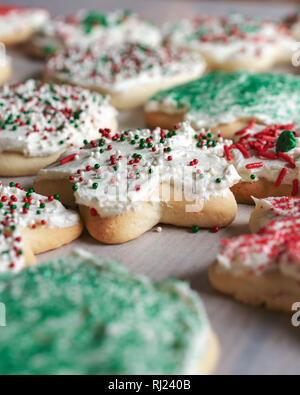 Various sugar cookies on parchment paper.  Frosted with white frosting and various christmas sprinkles.  Close up side view. Stock Photo