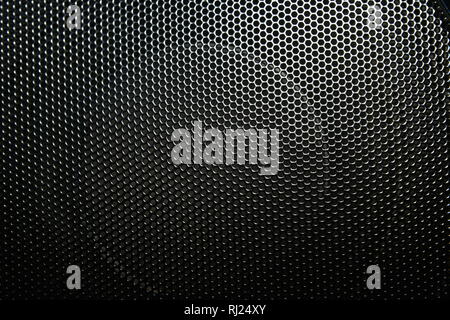 The speaker of a musical column hidden behind a grid with a pattern of rhythmically arranged holes Grid music speakers. Stock Photo