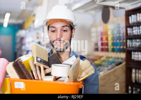 Young workman holding basket with picked tools in paint store Stock Photo