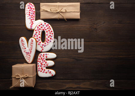 Close up of red and white gingerbreads hearts, word 'Love' and little boxes with presents. Festive decoration for Valentines day on brown wooden backg Stock Photo