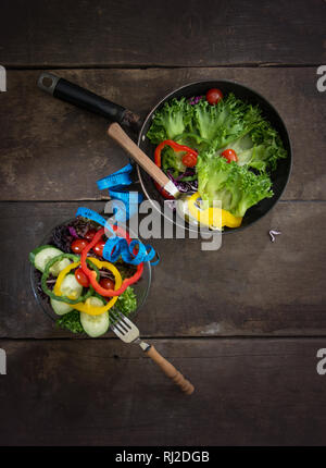 Fresh vegetables salad on the pan and bowl with measuring tape over wooden background. Diet Food and healthy lifestyle concept. Stock Photo