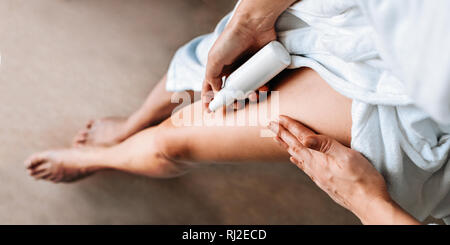 Body care. A young woman in the bathroom applies natural cream to her legs. Anti-cellulite care Banner Stock Photo