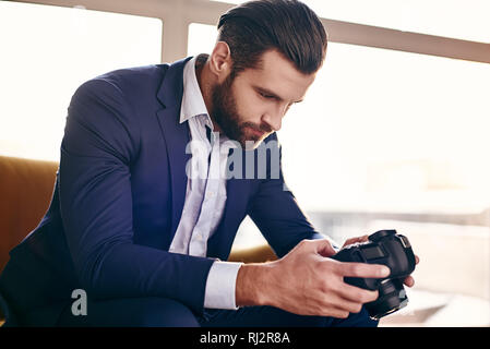 Close-up portrait of handsome young businessman in fashion suit who is looking at pictures on camera while sitting on sofa at office Stock Photo
