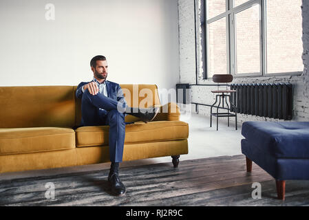 Feeling relaxed...Handsome and stylish young businessman is resting on sofa and thinking about business ideas. Fashion portrait. Business look. Stock Photo