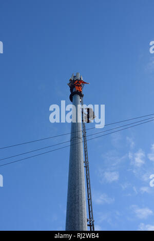 Two telecoms engineers working at height on 5g mobile phone mast with blue sky in bury lancashire uk Stock Photo