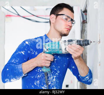 Portrait of young handyman using electric drill in repairable room Stock Photo