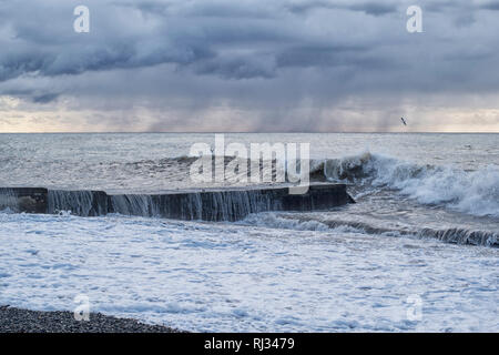 Seascape with a concrete pier during a storm in the rain with flying seagulls Stock Photo