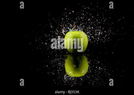 Sparkling water falls on juicy  green apple which stands on black table Stock Photo