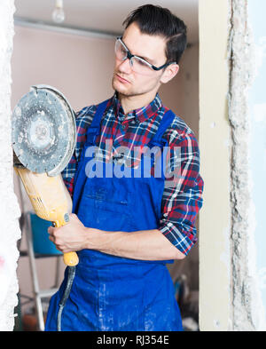 serious construction worker cutting concrete wall by using handheld circular saw in repairable room Stock Photo