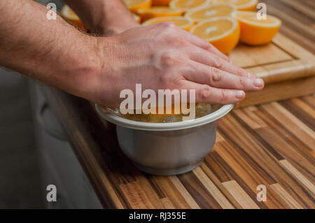 Squeezing oranges to make a fresh and natural juice. Closeup on man making fresh orange juice. Oranges and juicer on the wooden cutting board Stock Photo