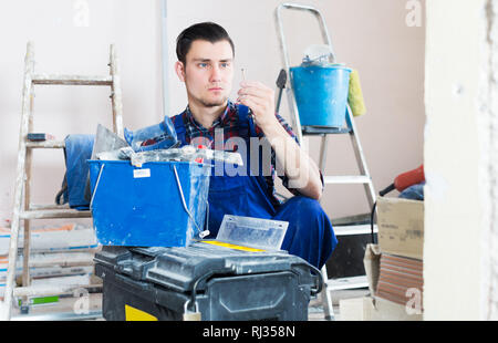 Positive adult worker repairing room and looking for necessary tool in toolbox Stock Photo