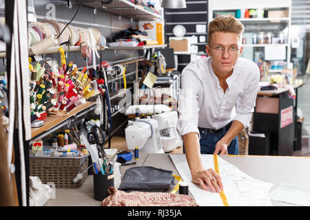 Young male tailor creating  pattern on table at sewing atelier Stock Photo