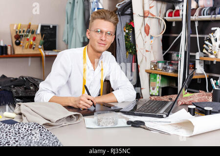 Confident  male  tailor using laptop and graphics tablet for creating pattern at sewing atelier Stock Photo