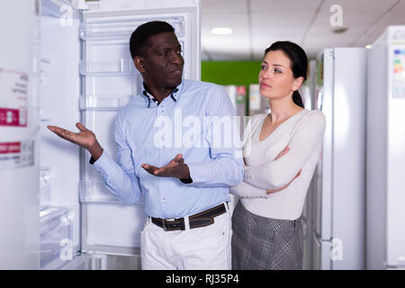 positive couple choosing fridge in store of household appliances Stock Photo