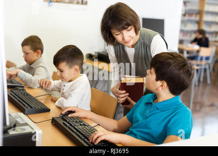 Friendly woman teacher helping tween boy during lesson in computer room of school library Stock Photo